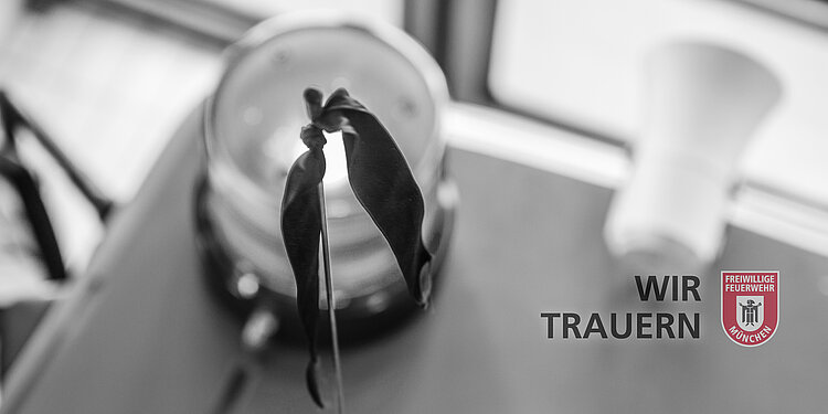 Trauerflor an einem Feuerwehrfahrzeug vor unscharfem Hintergrund mit Text 'WIR TRAUERN' und Logo der Freiwilligen Feuerwehr München